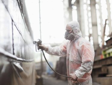 Worker spray-painting boat in shipyard